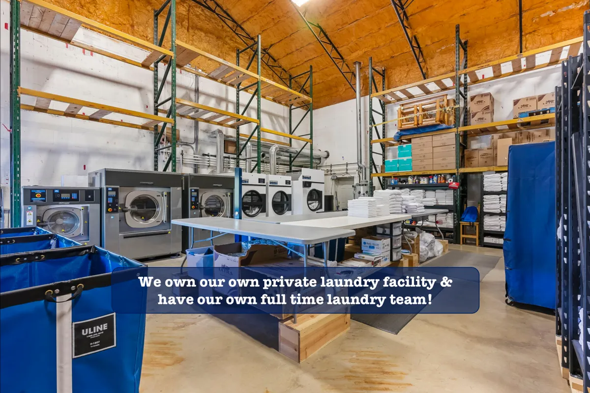A bright, efficient laundry area featuring industrial washing machines, a spacious folding table, and organized laundry baskets, all arranged in a clean, well-lit environment.