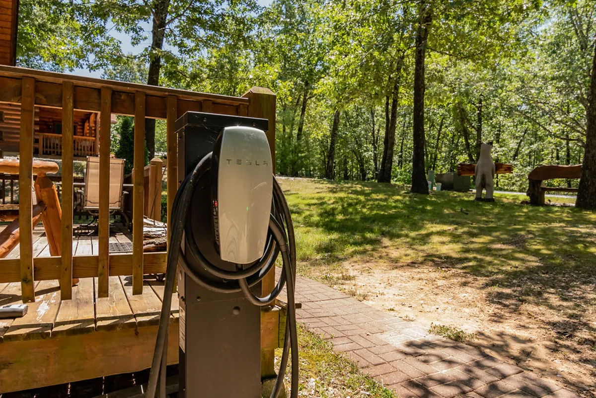 An exterior view showing a Tesla charging station nestled beside a wooden deck, surrounded by natural greenery—highlighting the rare amenity of EV charging in a rustic setting.